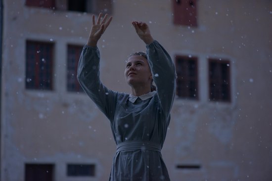 Jong meisje in grijs, lang jurkje met witte kraag, danst in de sneeuw.