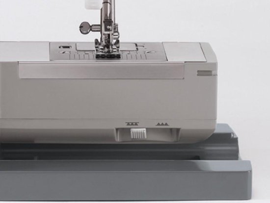 Grijze Singer naaimachine, detail van de onderkant met schuifregelaar en plastic voetstuk.