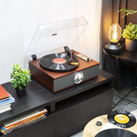 Retro platenspeler in een woonkamer op een donkere kast, met een stapel boeken en een plant ernaast.