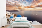 Behang - Fotobehang Zonsopkomst boven het water in Oia Griekenland - Breedte 600 cm x hoogte 400 cm