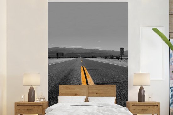 Behang - Fotobehang Zwart-wit foto van een weg met gele lijnmarkeringen - Breedte 145 cm x hoogte 220 cm