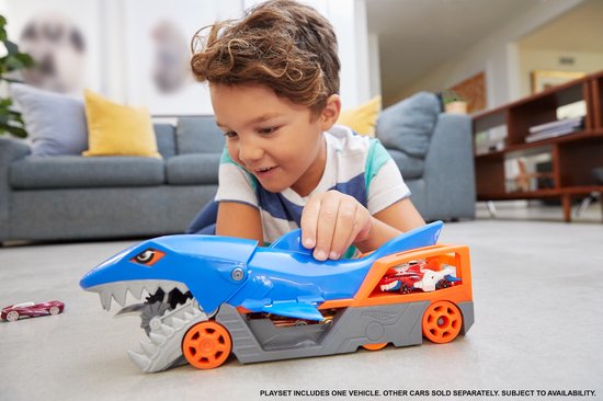 Jongen speelt met blauwe Hot Wheels haaienauto transporteur, laadt rode en witte auto's.