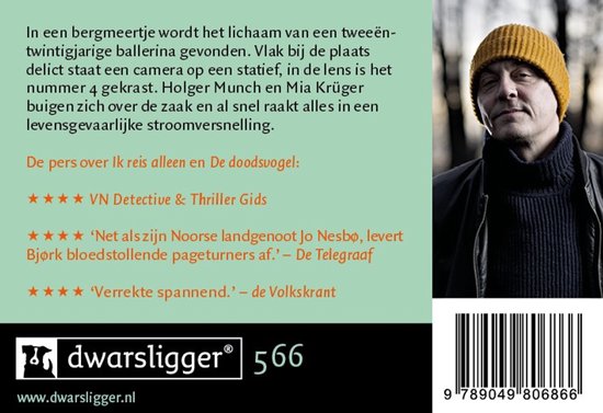 Close-up van een man met een geel mutsje, zwart colbert en donkere jas. Hij kijkt serieus in de camera.