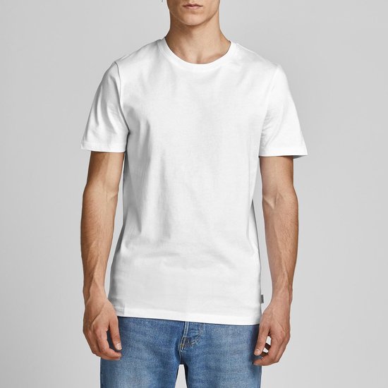 Man in een wit T-shirt en blauwe spijkerbroek, staand met een lichte draai.
