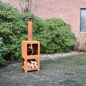 Roestkleurige stalen buitenkachel met brandend haardvuur en houtblokken op de onderste plank, staand op een betegeld terras.