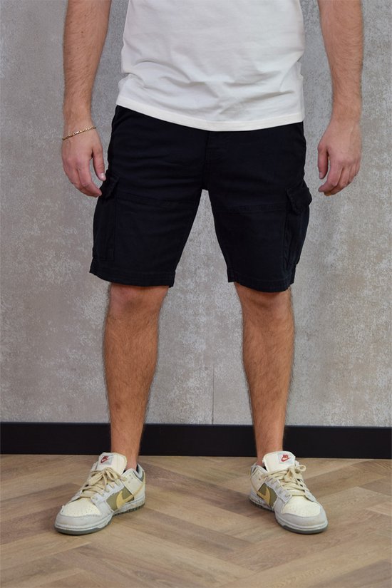 Man in zwarte cargobroek met klepzakken, gedragen met een witte top en sneakers.