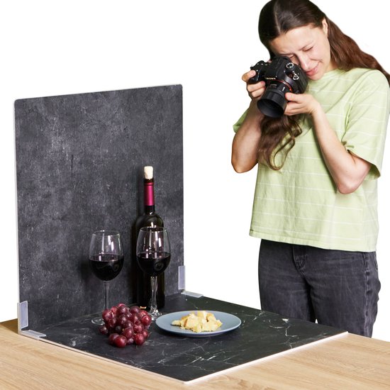 Vrouw fotografeert wijn, kaas en druiven op een zwarte marmeren achtergrond met steenprint.