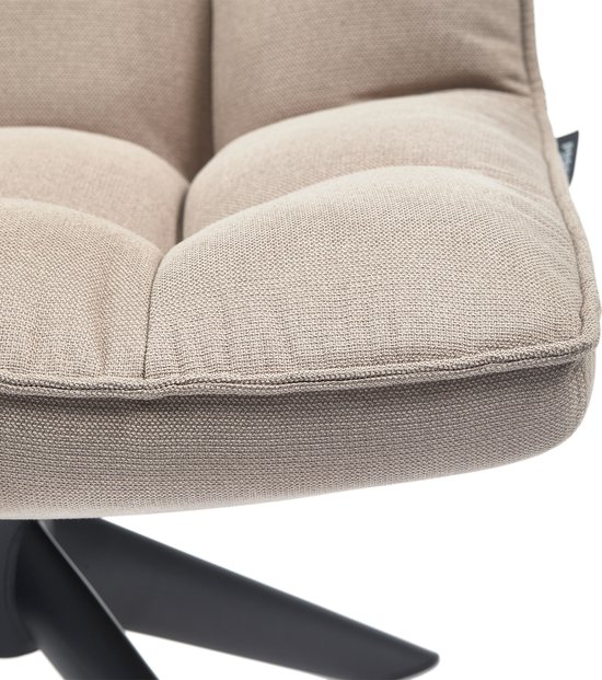 Close-up van de gewatteerde zitting van een zandkleurige fauteuil met zichtbare naden.