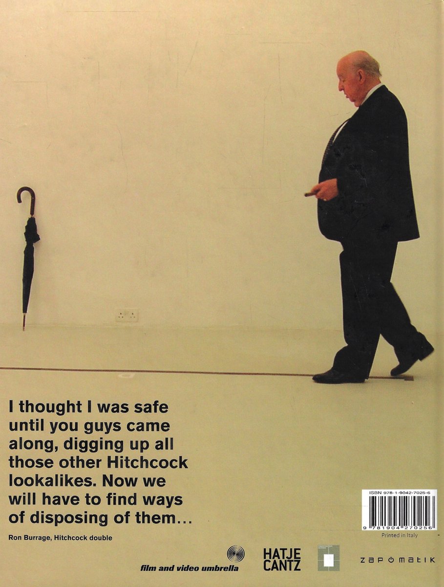 Een man in een zwart pak, Ron Burrage, een Hitchcock-double, loopt langs een bruine lijn op een witte muur. Een zwarte paraplu staat ernaast. Tekst: "I thought I was safe until you guys came along, digging up all those other Hitchcock lookalikes. Now we will have to find ways of disposing of them..."