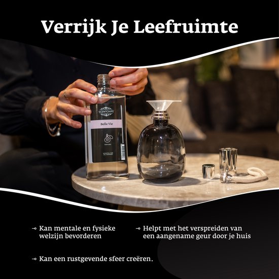 Een hand wordt gebruikt om een glazen fles geurolie 'Belle Vie' in een glazen diffuser te gieten.
