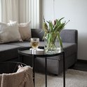 Set de six sous-verres ronds aspect marbre dans un support noir sur une table d'appoint, à côté d'un verre et d'un vase à fleurs.
