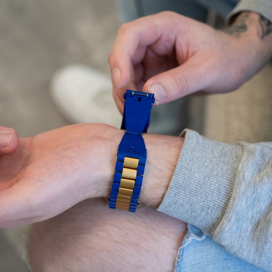 Hand van een persoon die een Apple Watch met een blauw en goudkleurig metalen bandje bevestigt.
