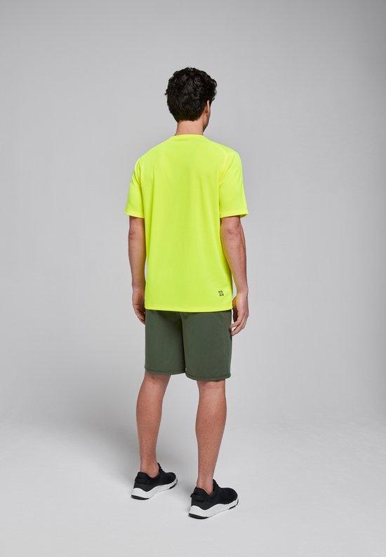 Man in limegroen sportshirt en donkergroene sportbroek, van achteren gezien.