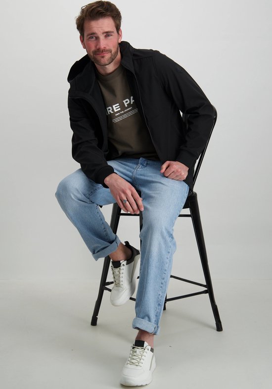 Man zittend in een zwarte jas, met lichtblauwe jeans.