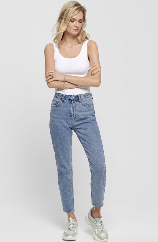 Model draagt een witte tanktop met spaghettibandjes en een spijkerbroek.