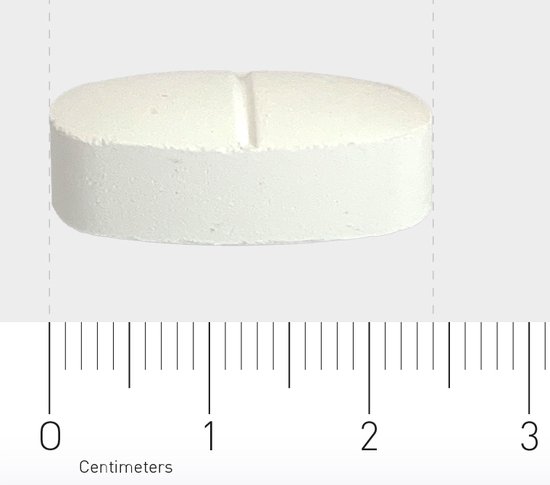 Close-up van een witte Orthica Magnesiumcitraat-tablet met een deelstreep, met een liniaal die de grootte aangeeft in centimeters.