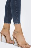 Close-up van de enkels van een model in beige sandalen en donkerblauwe skinny jeans met rafels.