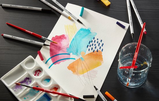 Een aquareltekening met kleurvlakken en lijnen, omringd door teken- en schildermaterialen zoals penselen en stiften.