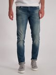 Man draagt een blauwe spijkerbroek met lichte wassing en omgerolde broekspijpen. Slim fit.