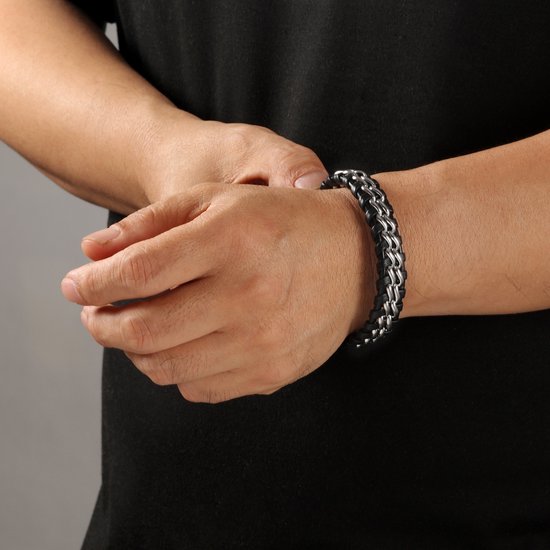 Man draagt zwarte gevlochten leren armband met dubbele zilverkleurige schakelketting om pols.