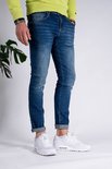 Man met donkerblauwe slim fit spijkerbroek met opgerolde pijpen en witte sneakers.