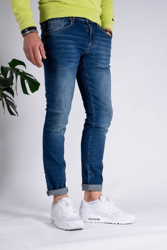 Man met donkerblauwe slim fit spijkerbroek met opgerolde pijpen en witte sneakers.