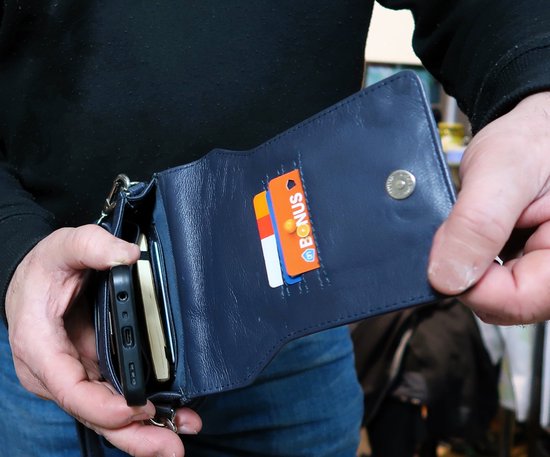 Man houdt donkerblauwe leren tas open, met pasjes en telefoon erin.