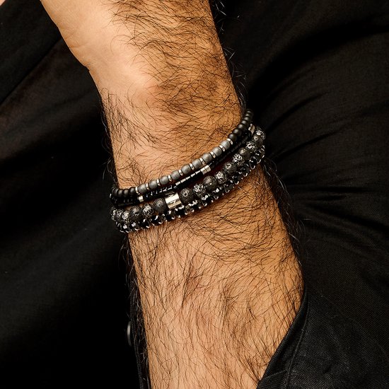 Een mannenpols met drie zwarte kralenarmbanden, waaronder lava-kralen, mat-hematiet en een zilverkleurige schakel.