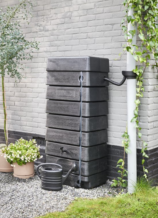 Zwarte stapelbare regenton met kraantje en gieter ernaast, naast een regenpijp aan een grijze bakstenen muur.