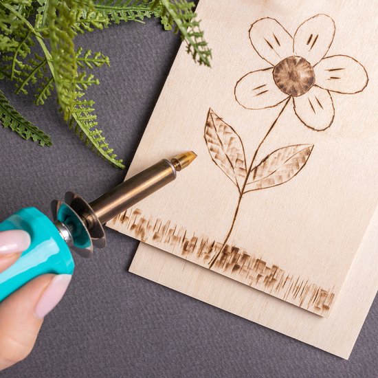 Hand met pyrografie pen bij berken multiplex plaat met bloemenontwerp.