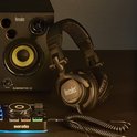 Zwarte DJ-koptelefoon met Hercules-logo, naast een DJ-monitor luidspreker en mixer.