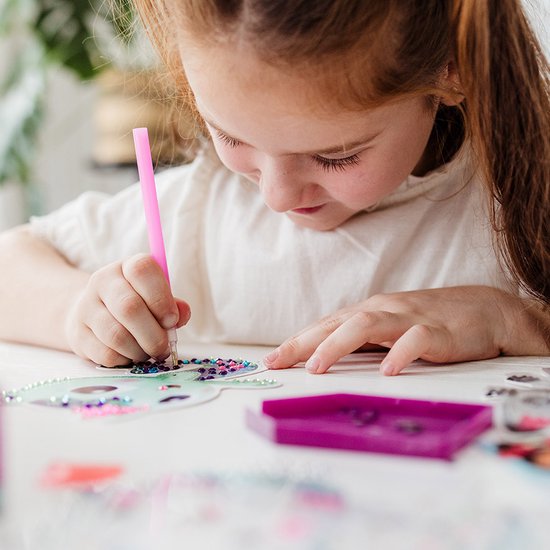 Meisje met rood haar maakt een diamant schilderij met een roze pen.