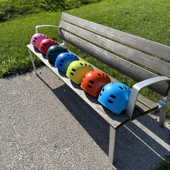 Sept casques PRO SPORT LIGHTS colorés sur un banc en bois dans l'herbe: rose, rouge, vert, bleu, jaune, orange, bleu clair.