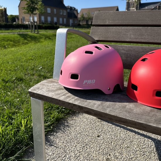 Casque rose avec logo "PRO SPORT LIGHTS", sur un banc en bois avec de l'herbe verte en arrière-plan.
