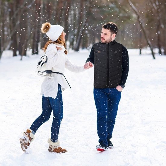 Man in zwarte bodywarmer houdt hand vast van vrouw in witte winterkleding in besneeuwde omgeving.
