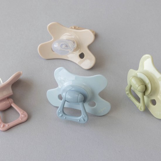 Vier Difrax fopspenen in verschillende pastelkleuren: roze, blauw, beige en groen.