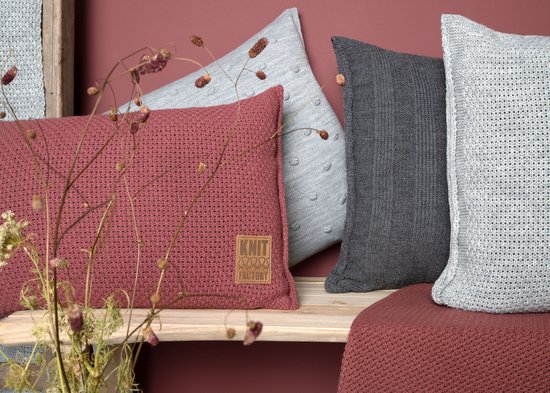Coussins tricotés gris clair, gris foncé et rose poudré, certains avec un motif grain, sur un banc en bois.