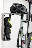 Zwart POC racefietshelm boven een zilverkleurig Stasdock-rek met een zwarte racefietsschoen met limegroene accenten, aan een racefiets.
