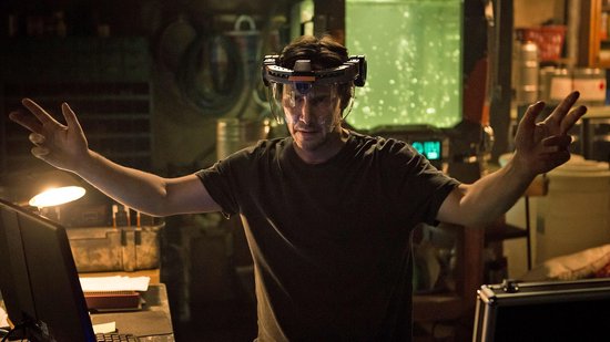 Keanu Reeves met een VR-bril op, handen uitgestoken in een werkplaats.