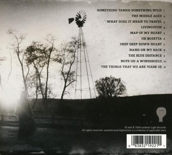 Een silhouet van een vrouw staat voor een windmolen in een veld met bomen. Tracklist is zichtbaar.