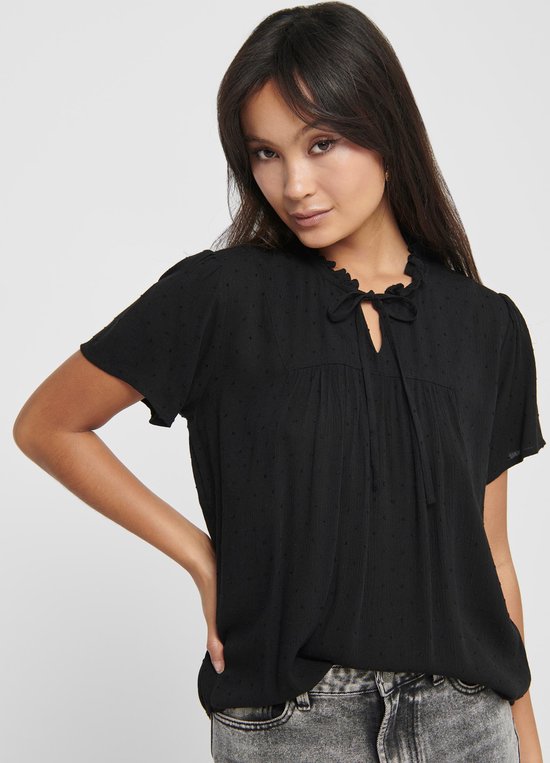 Zwarte blouse met korte mouwen, ruchekraag en strikdetail bij de hals. De stof heeft een subtiel stipjespatroon.