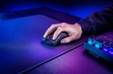 Een hand gebruikt een zwarte gamingmuis op een zwart gamingmuismat, met een verlicht toetsenbord op de achtergrond.