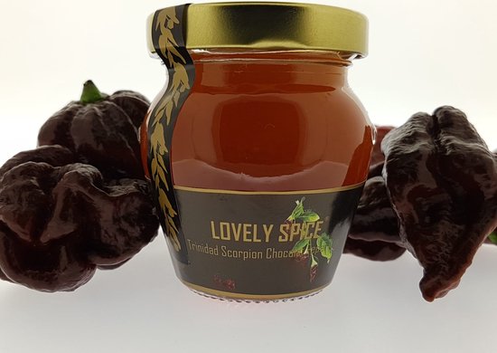 Lovely Spice Trinidad Scorpion Chocolat pepergelei in een glazen potje met goudkleurig deksel, omringd door donkere pepers.