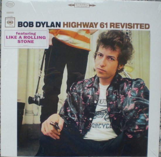 Bob Dylan met een zwart-roze panterprint jasje, een wit T-shirt met "Motorcycle" erop, en zwarte broek. Met sticker "Featuring Like A Rolling Stone".