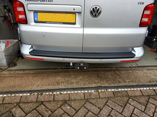 Achterkant van zilverkleurige Transporter met nummerplaat NL, trekhaak en zwarte bumperbeschermer met rode reflectors.