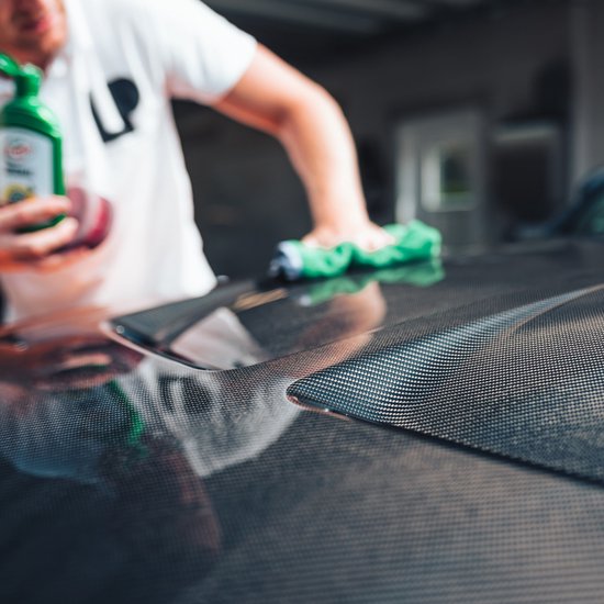Man met witte polo poetst auto met groene microvezeldoek en Turtle Wax fles.