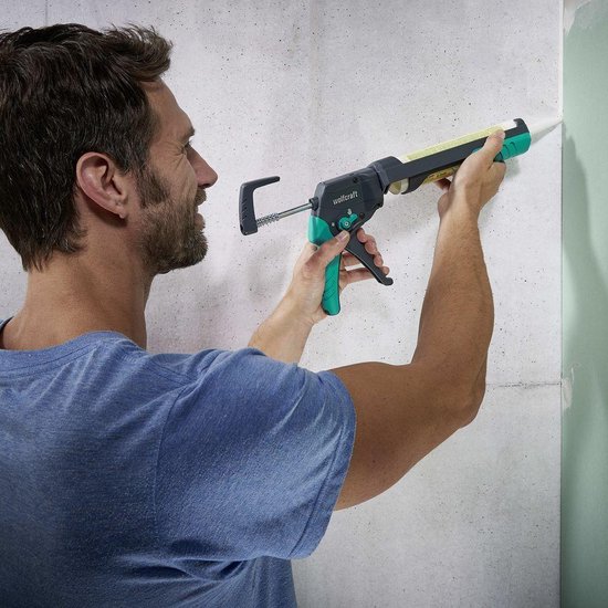 Man in blauw shirt gebruikt een wolfcraft kitpistool met groene en zwarte accenten om een muur af te kitten.