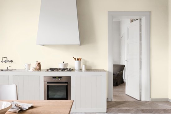 Lichte keuken met witte keukenkastjes, kookplaat, afzuigkap en een open deur naar een kamer.