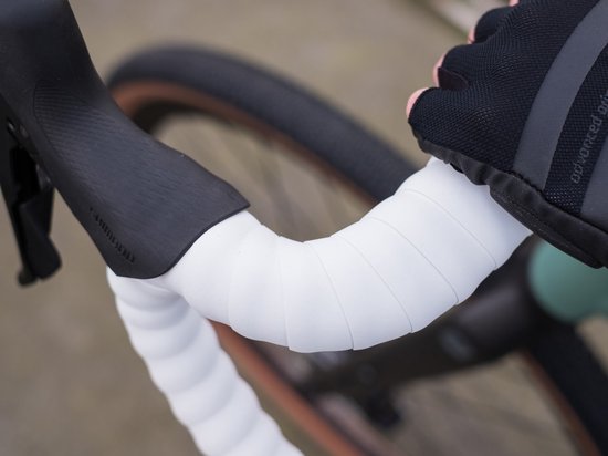 Hand met zwart fietsstuur met witte stuurlint en Shimano versnellingen.