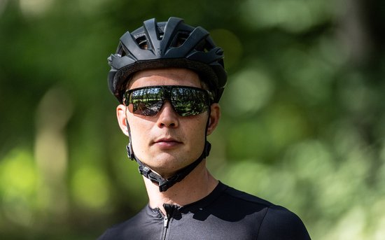 Man met zwarte fietshelm en sportbril met gespiegelde glazen, kijkt naar de camera.
